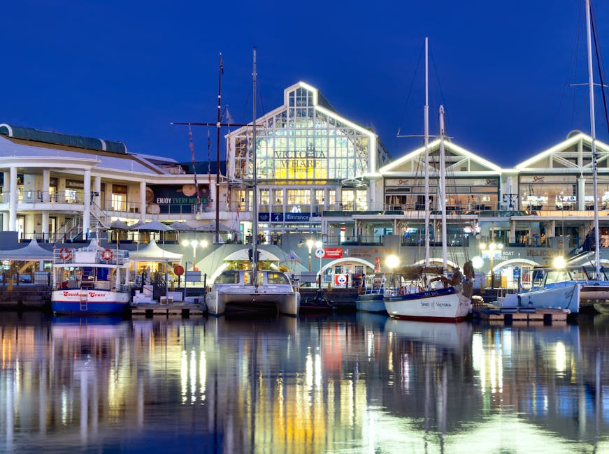 Illuminated view of Victoria Wharf Shopping Centre surrounded by yachts and boats at night in Cape Town, South Africa.
