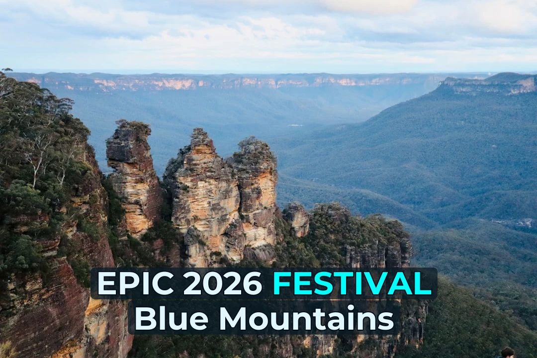 a rocky cliff with trees and a valley below with Three Sisters in the background